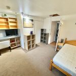 Furnished single bedroom with wooden bed and shelves.