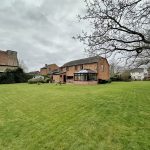 Spacious garden with brick house in overcast weather.
