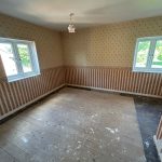 Empty room with patterned wallpaper and wooden floor.