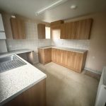 Empty kitchen with wooden cabinets and tiled walls.