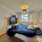 Bedroom with floral wallpaper, TV, and cat on bed.