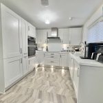 Modern white kitchen with appliances and chevron flooring.