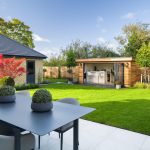 Modern garden with patio, greenery, and wooden garden room.