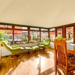Bright conservatory with green chairs and dining table.