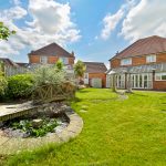 Sunny garden with pond and two detached houses.