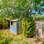 Blue wooden garden shed surrounded by trees.