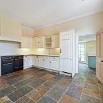 Spacious kitchen with cream cabinets and stone floor.