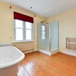 Bathroom with bathtub, shower, and wooden floor.