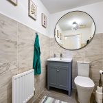 Modern bathroom with circular mirror and grey cabinet.