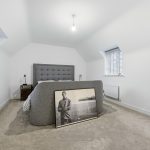 Modern bedroom with grey bed and framed photograph.