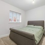 Minimalist bedroom with grey bed and window blinds.
