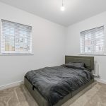 Minimalist bedroom with grey bedding and windows.