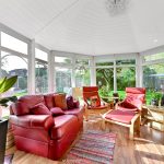 Sunlit conservatory with red sofas overlooking garden.