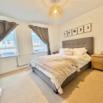 Modern bedroom with grey bed, wooden furniture.